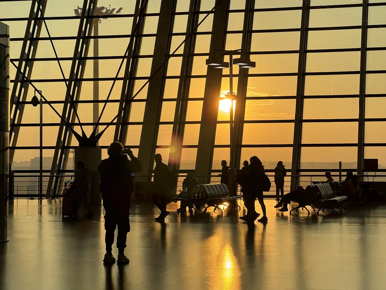 Passengers in silhouette at a terminal window of Shanghai Pudong International Airport at sunset