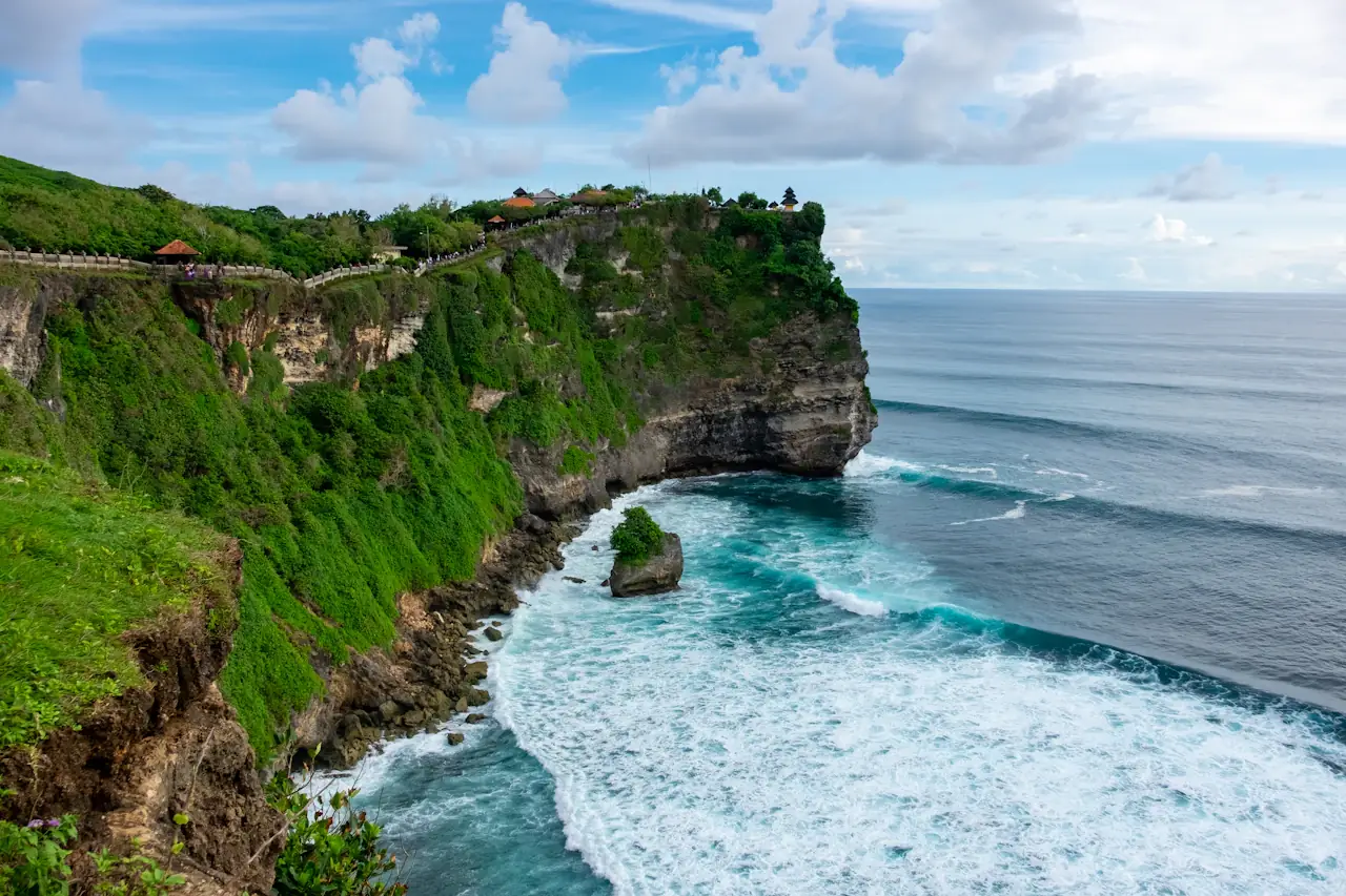 The green cliffs of Uluwatu in Bali with white surf below and clouds above