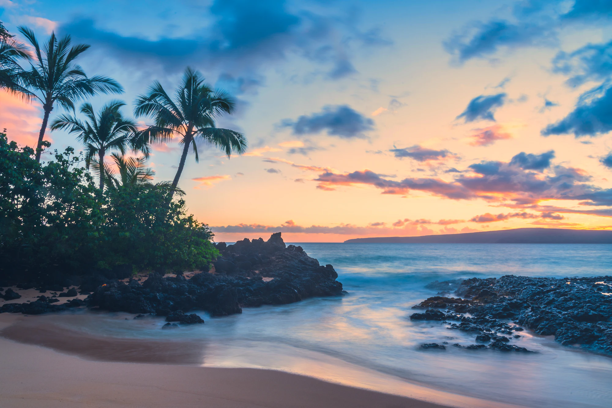 A secluded cove beach on Maui at sunset, palms and surf