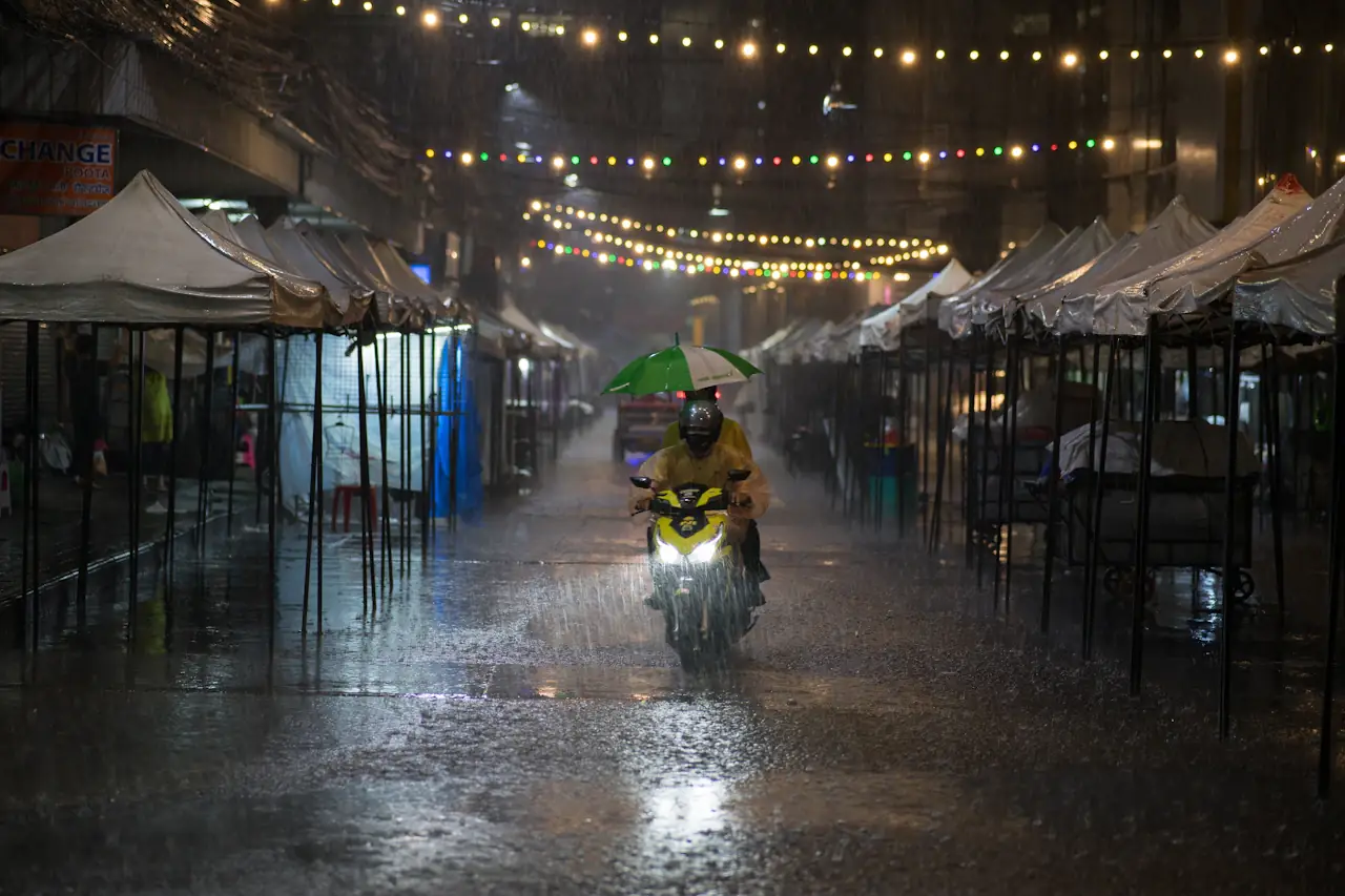 A motorbike on a rain-soaked Bangkok street between night-market awnings and string lights