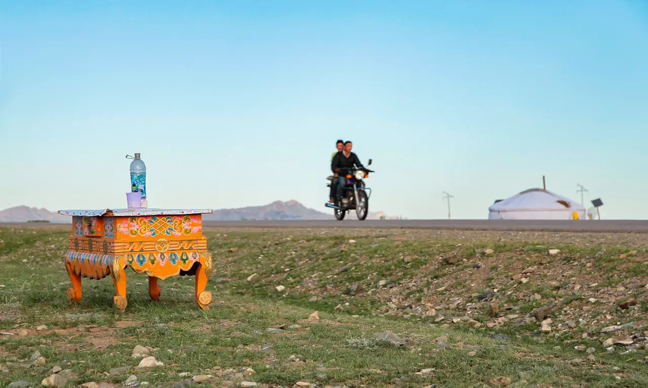 A motorbike passing a roadside milk station and a ger on the open road in central Mongolia