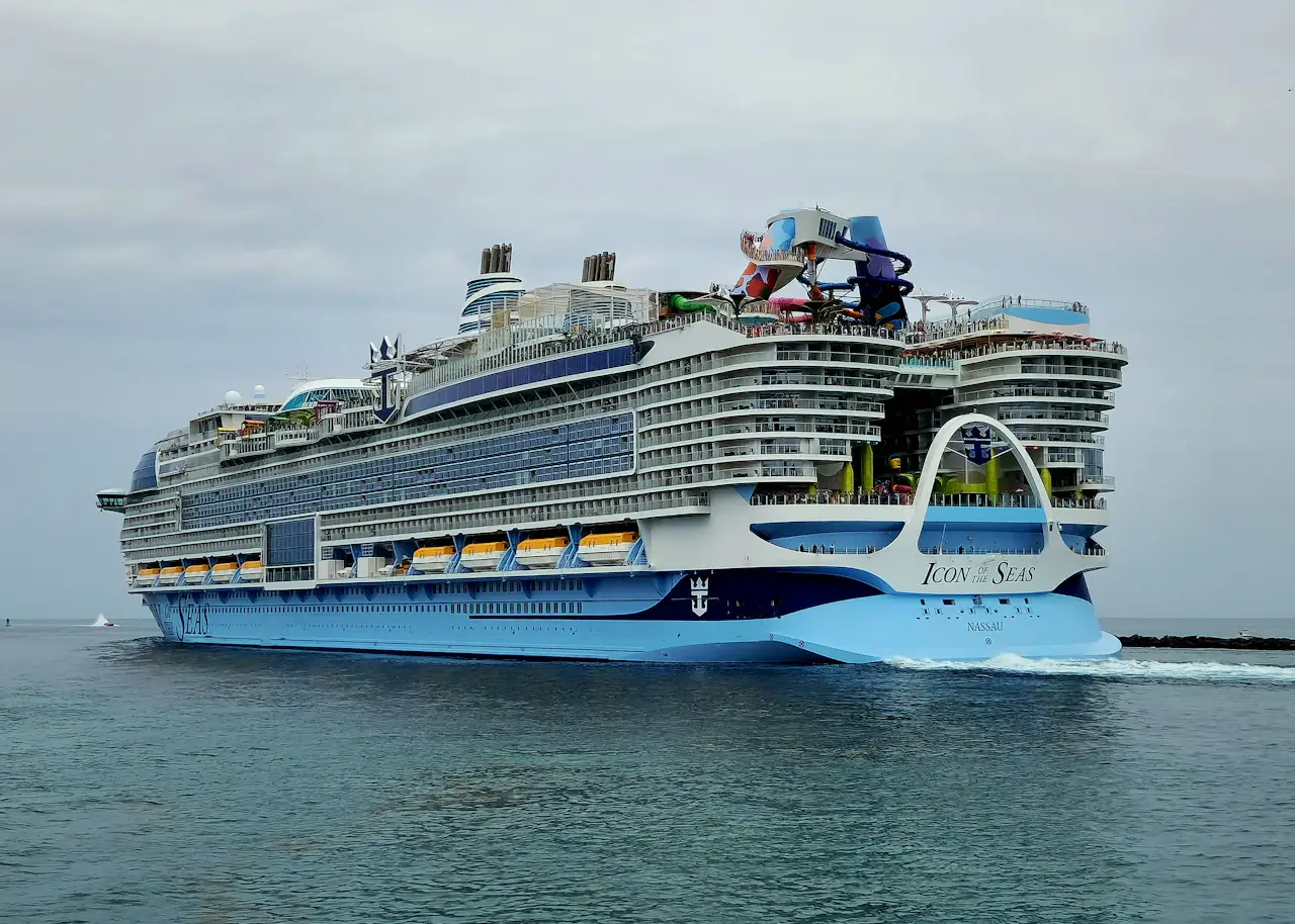 皇家加勒比 Icon of the Seas 驶出迈阿密港，蓝白船身，船尾拱形结构和上层水滑道清晰可见