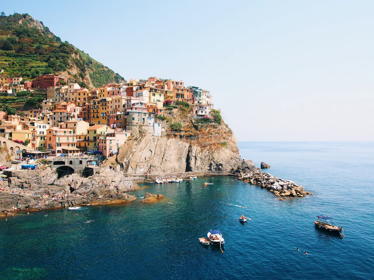 A colourful Italian seaside village on cliffs above blue water, small boats below