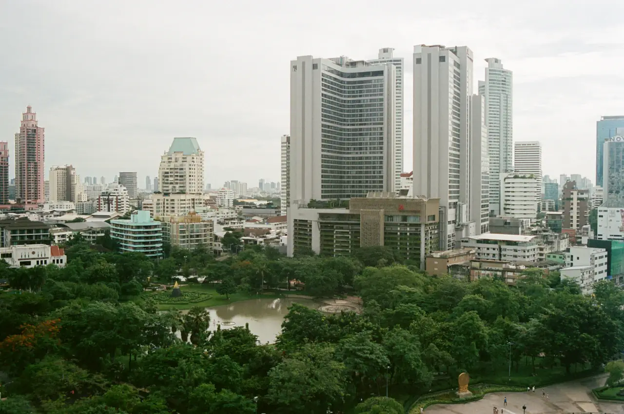 High-rise buildings above a green city park in Bangkok under a pale sky
