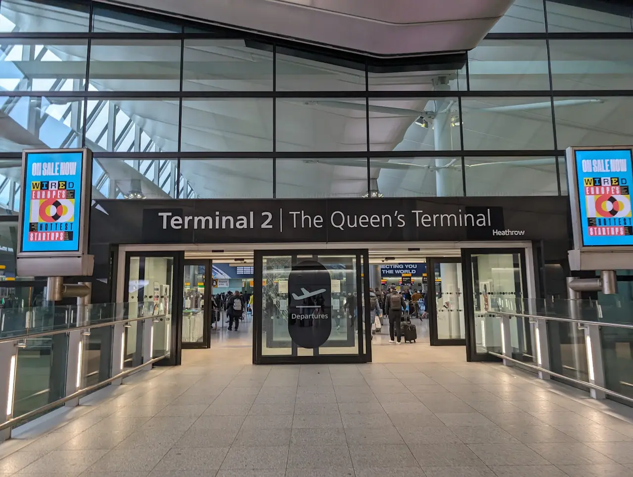 希斯罗机场 2 号航站楼出发入口，门楣写着 Terminal 2，两侧各有一块广告屏